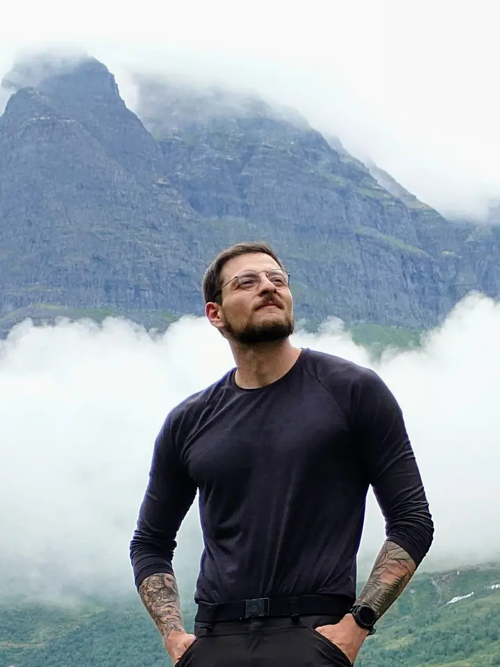 Sergio Gutierrez standing on a grassy ridge, a cloud-wrapped mountain peak behind him